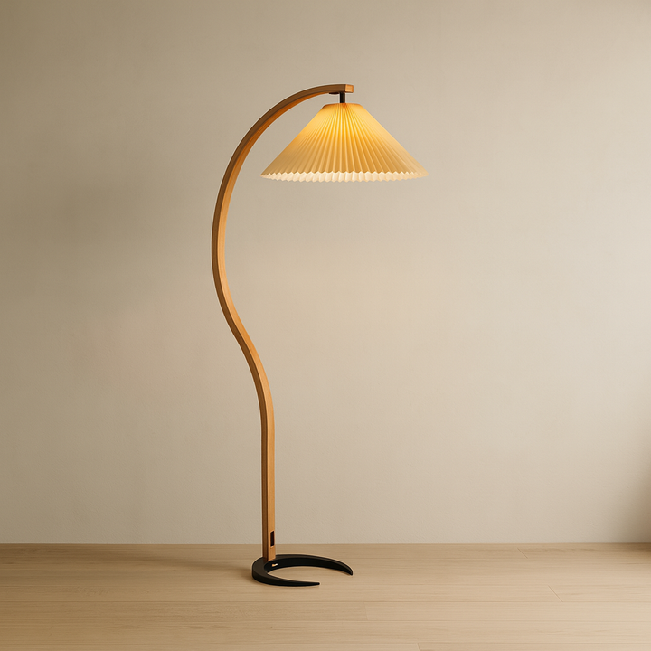 Curved floor lamp with pleated shade on a wooden floor against a beige wall